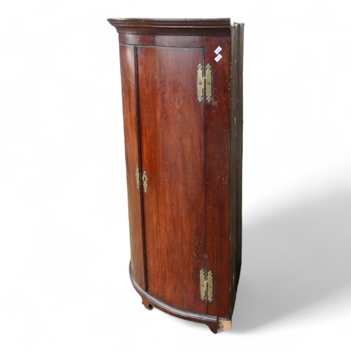 973 - A George III mahogany bowfront corner cupboard - the moulded cornice above a pair of doors enclosing... 