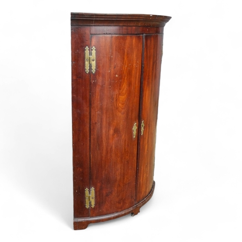 973 - A George III mahogany bowfront corner cupboard - the moulded cornice above a pair of doors enclosing... 