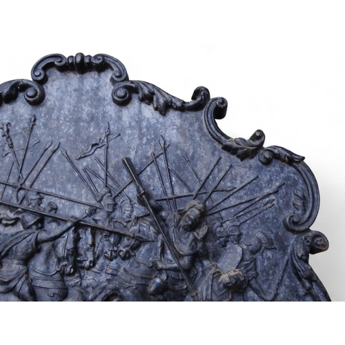 25 - A 19th century cast iron fire back - the relief scene showing an ancient battle within a scrolled ca... 