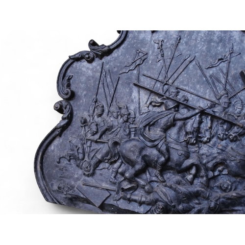 25 - A 19th century cast iron fire back - the relief scene showing an ancient battle within a scrolled ca... 