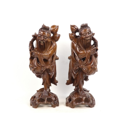 307 - A pair of 20th century carved hardwood deities - each holding a staff with fruit, 40cm high. (2)