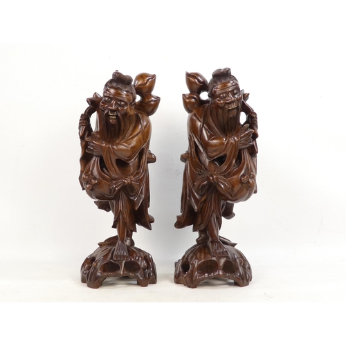 307 - A pair of 20th century carved hardwood deities - each holding a staff with fruit, 40cm high. (2)