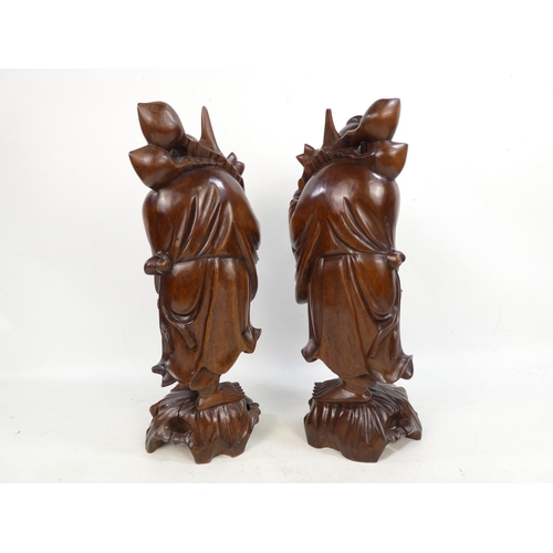 307 - A pair of 20th century carved hardwood deities - each holding a staff with fruit, 40cm high. (2)