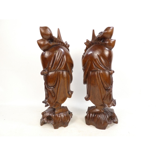 307 - A pair of 20th century carved hardwood deities - each holding a staff with fruit, 40cm high. (2)