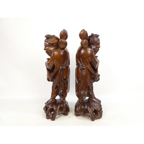 307 - A pair of 20th century carved hardwood deities - each holding a staff with fruit, 40cm high. (2)