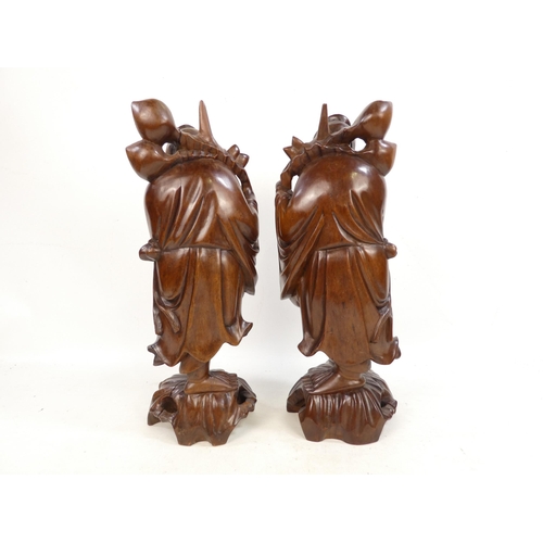 307 - A pair of 20th century carved hardwood deities - each holding a staff with fruit, 40cm high. (2)