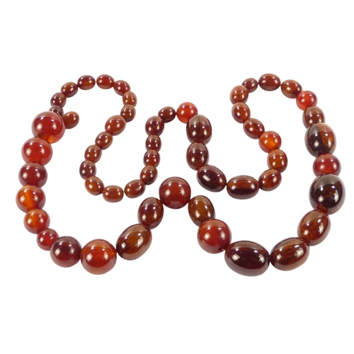 616 - A string of graduated oval cherry 'amber' beads - length 80cm.