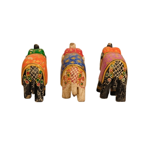 111 - Three polychrome painted elephants - one white and two black, with coloured blankets featuring gilt ... 