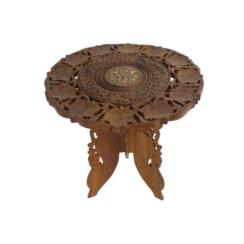 941 - An Indian hardwood occasional table - the pierced circular top carved with leaves, on a hinged trifo... 