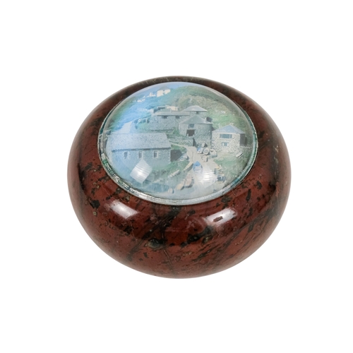 128 - A red serpentine souvenir paperweight - of circular form and decorated with an image of Cadgwith, 12... 