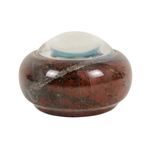 128 - A red serpentine souvenir paperweight - of circular form and decorated with an image of Cadgwith, 12... 