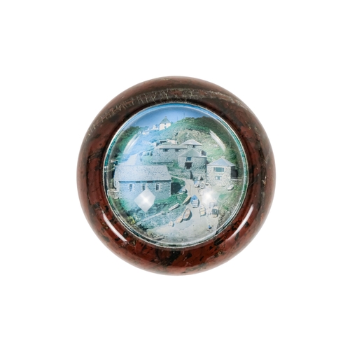 128 - A red serpentine souvenir paperweight - of circular form and decorated with an image of Cadgwith, 12... 