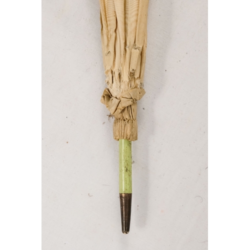 142 - An early 20th century white silk parasol - the green painted handle terminating in a carved rabbits ... 