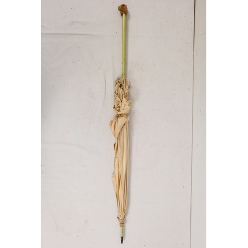142 - An early 20th century white silk parasol - the green painted handle terminating in a carved rabbits ... 