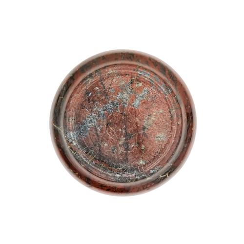 128 - A red serpentine souvenir paperweight - of circular form and decorated with an image of Cadgwith, 12... 