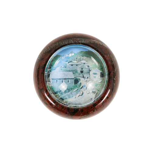 128 - A red serpentine souvenir paperweight - of circular form and decorated with an image of Cadgwith, 12... 
