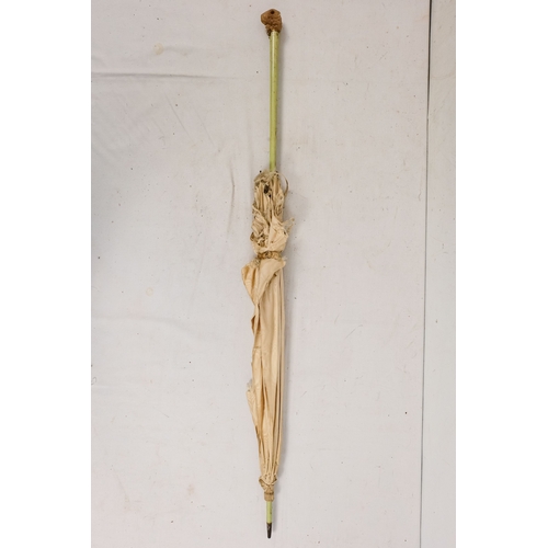 142 - An early 20th century white silk parasol - the green painted handle terminating in a carved rabbits ... 