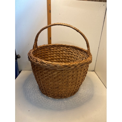 64 - Handwoven wicker basket with a single handle, featuring a natural finish and circular opening.