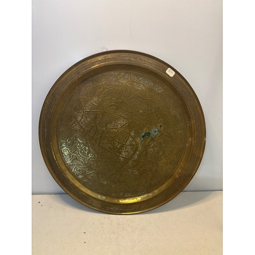 58 - Large circular brass tray featuring intricate engraved detailing and designs. Some patina and wear v... 