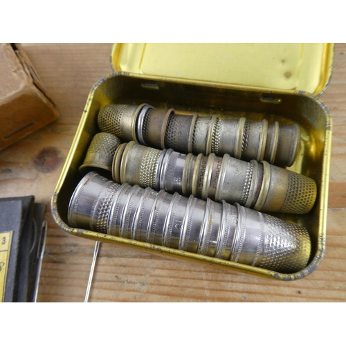 152 - An assortment of vintage thimbles and a vintage cardboard box containing sewing needles and more.