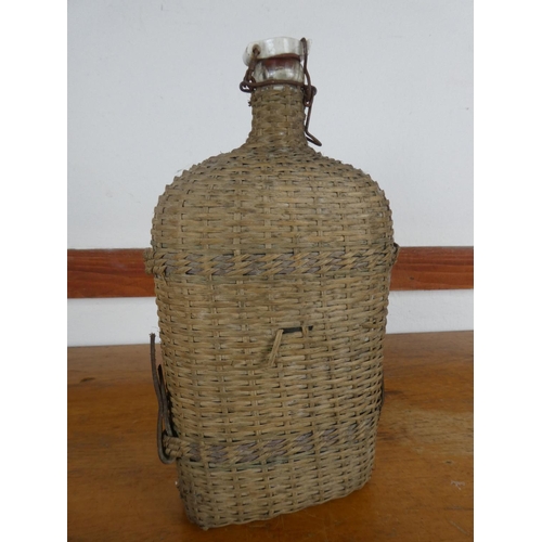 77 - An antique wicker covered bottle with ceramic stopper, measuring 31cm tall.