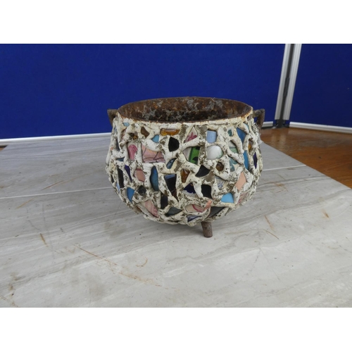 913 - An antique cast iron three legged pot decorated with coloured cut glass and ceramics.