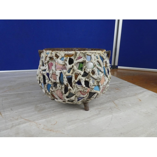 913 - An antique cast iron three legged pot decorated with coloured cut glass and ceramics.