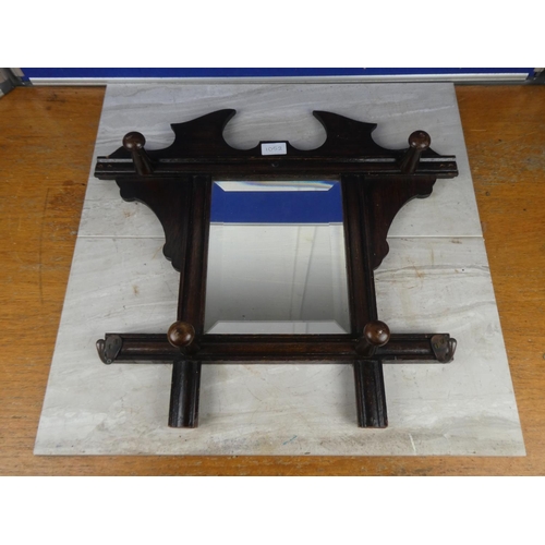 1052 - An oak framed wall mirror with clothes hooks.