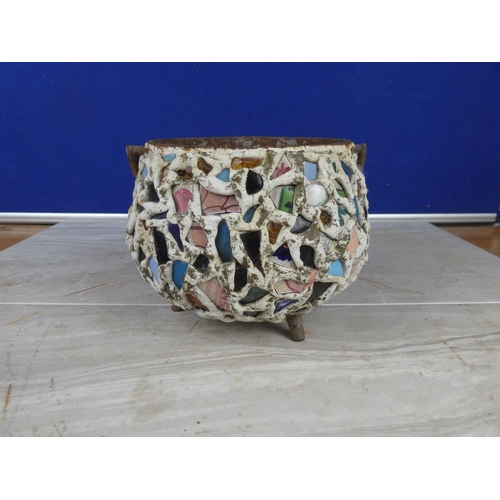 913 - An antique cast iron three legged pot decorated with coloured cut glass and ceramics.