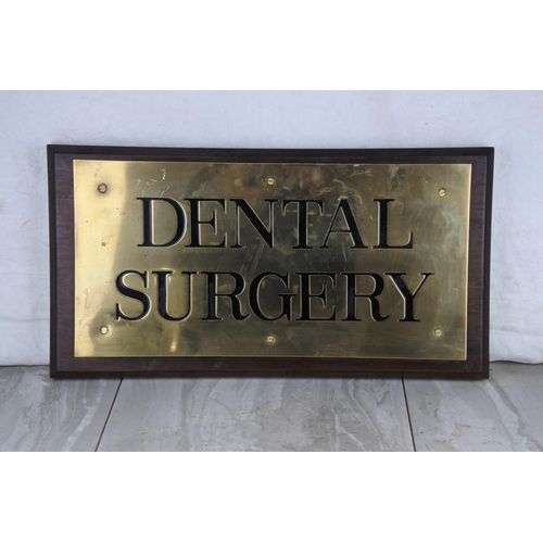 73 - A large wooden and brass wall plaque 'Dental Surgery'. Approx 25x46cm.