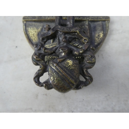 329 - A brass door knocker in the style of a house with crest.