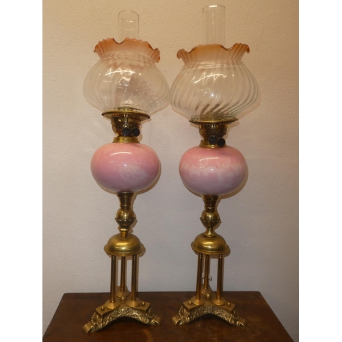 118 - A stunning pair of antique brass oil lamps with pink marble glaze fonts, measuring 29