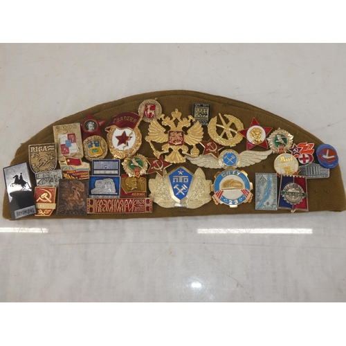 163 - A USSR military cap with a large collection of assorted badges.