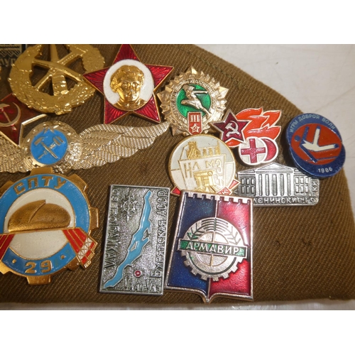 163 - A USSR military cap with a large collection of assorted badges.