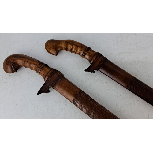 568 - Pair of intricately carved wooden machetes with ornate handles and scabbards. Traditional craftsmans... 