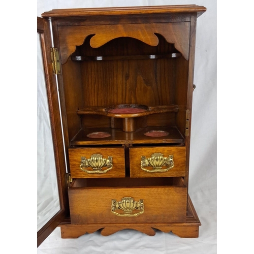 72 - An antique oak smoker's cabinet with a glass door and three brass-handled drawers. Interior shelves ... 