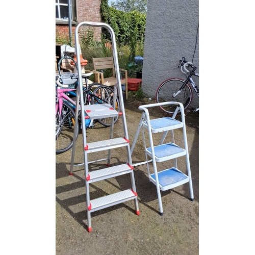 658 - Set of two metal step ladders. One ladder has four steps and the other has three steps.