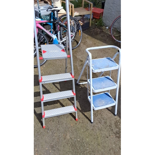 658 - Set of two metal step ladders. One ladder has four steps and the other has three steps.