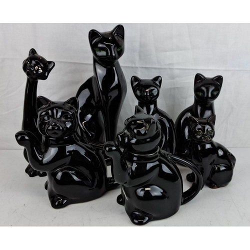 12 - A collection of black ceramic cat figurines. The figurines showcase intricate detailing with green e... 