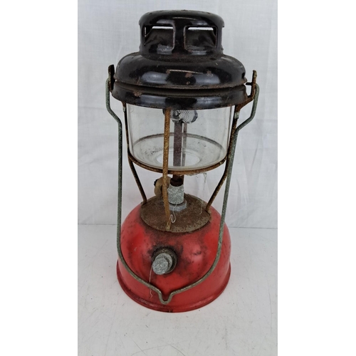 33 - Vintage red and black kerosene lantern with metal frame and glass chimney, showing a rustic, weather... 