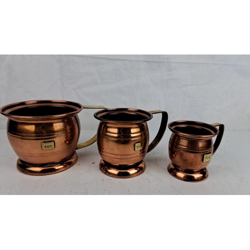 57 - Set of three vintage copper measuring jugs with brass handles. Marked capacities: 1 QT, 1 PT, and 1/... 