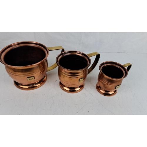 57 - Set of three vintage copper measuring jugs with brass handles. Marked capacities: 1 QT, 1 PT, and 1/... 