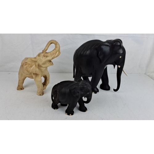 64 - Three carved elephant figurines, varying in colour and size.