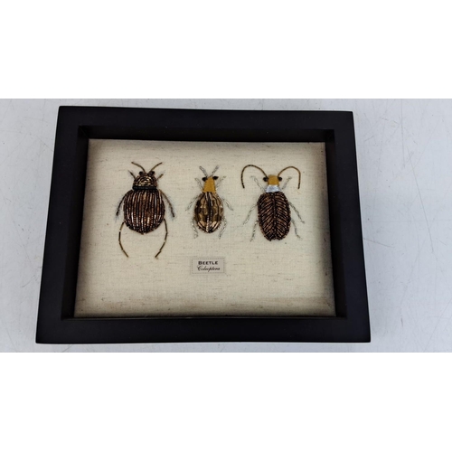 91 - Framed artwork displaying three beaded beetle designs on a fabric linen background, labeled 