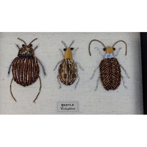 91 - Framed artwork displaying three beaded beetle designs on a fabric linen background, labeled 