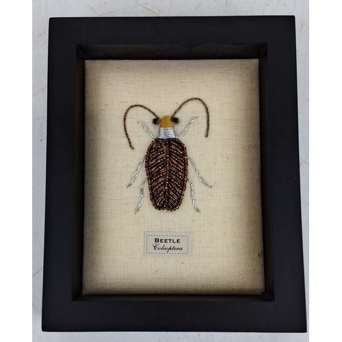 93 - Framed beetle artwork with intricate bead detailing on a fabric linen background. Labelled 