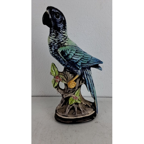 240 - Hand-painted ceramic parrot figurine perched on a branch, featuring vibrant blue and green feathers.... 