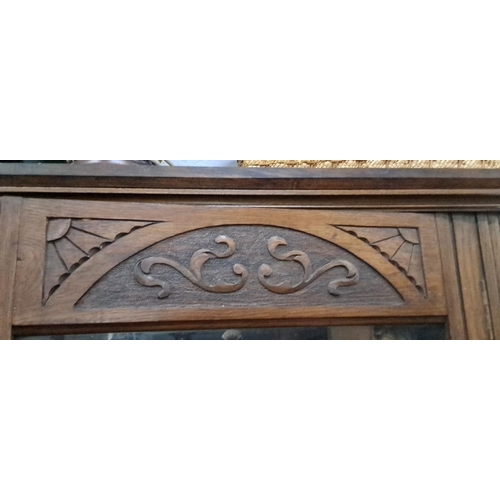 21 - Ornately carved oak display cabinet. It features glass doors and intricate scroll work details. It i... 