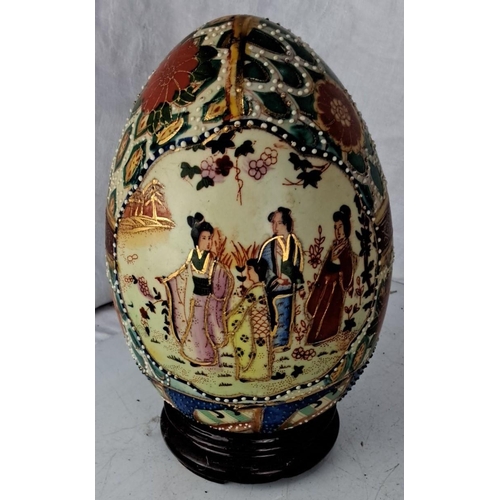 84 - Hand-painted porcelain egg with intricate floral and figurative designs, complemented by a wooden st... 