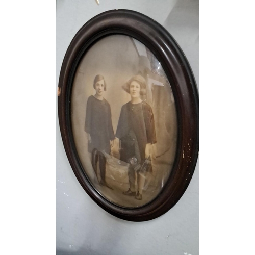 497 - Oval sepia photograph of two young women in dark clothing, housed in a dark wooden frame from the ea... 